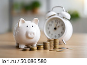 A piggy bank sits on a table next to a clock. Стоковое AI-изображение, AI-художник Ярославский Максим / Фотобанк Лори