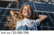 A young girl is laying on a solar panel, smiling and looking up at the sky. Стоковое AI-изображение, AI-художник Ярославский Максим / Фотобанк Лори