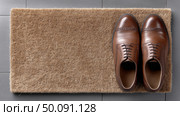 Brown dress shoes neatly placed on a doormat at home entrance. Стоковое AI-изображение, AI-художник Katsiaryna Repich / Фотобанк Лори