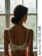 A woman with her back turned showcases a stylish bra, highlighting the delicate details. Soft natural light enhances the allure of this intimate moment, captured indoors Generative AI. Стоковое AI-изображение, AI-художник Юлия Петровская / Фотобанк Лори