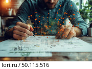 A contemporary conceptual image that combines reality and digital visualization. In the foreground, a man writes or draws on paper, concentrating on a project. An abstract visualization of a data network is superimposed on the scene - orange dots connected by lines symbolize information flows, neural networks or data processing technologies. The atmosphere emphasizes the synergy of engineering and digital technologies, ideal for themes of artificial intelligence, analytics, design and scientific research. Стоковое AI-изображение, AI-художник Анна Кривицкая / Фотобанк Лори