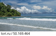 The waves of the turquoise ocean are foaming and spreading across the beach. A hill with green tropical vegetation in the distance. Blue sky, picturesque cumulus clouds. Malaysia. Borneo.Kota Kinabalu. Стоковое фото, фотограф Вера Ивановна Кубарева / Фотобанк Лори