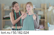Woman tailor with a client trying on a sample of a sewn dress. Female client checking the size and quality of the dress in the sewing workshop. Стоковое видео, видеограф Яков Филимонов / Фотобанк Лори