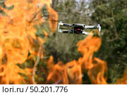 Flying drone Quadcopter with camera pointed at viewer outdoor in a fire in the foreground spurts of flame forest background. Стоковое фото, фотограф Camptoloma / Фотобанк Лори
