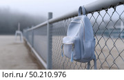 Backpack hanging on a fence at a deserted beach in foggy weather. Рюкзак висит на заборе на пустынном пляже в туманную погоду. Стоковое AI-изображение, AI-художник Katsiaryna Repich / Фотобанк Лори