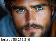 A close-up of an attractive young man with a thick beard and bright turquoise eyes. His face takes up almost the entire frame, which emphasizes the expressiveness of his gaze and the texture of his skin. The light is natural, warm, creating a feeling of coziness and openness. The man radiates confidence, strength and inner calm. This is a versatile portrait for themes related to male attractiveness, cosmetics, skin care, masculinity, fashion and charisma. Стоковое AI-изображение, AI-художник Анна Кривицкая / Фотобанк Лори