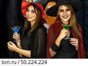 Two young adult and teenager girls celebrating a Halloween party carnival Festival in Halloween costumes drinking alcohol cocktail. Стоковое фото, агентство Ingram Publishing / Фотобанк Лори