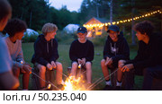 Friends gather around a campfire under the evening sky, enjoying roasted marshmallows and laughter in a forest setting. Стоковое AI-изображение, AI-художник Сергей Толмачёв / Фотобанк Лори