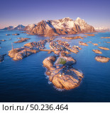Aerial view of rocks in sea, snowy mountains, purple sky at sunset in Lofoten Islands, Norway. Winter landscape with small islands in water, football field on the rock. Top view of Henningsvaer city. Стоковое фото, агентство Ingram Publishing / Фотобанк Лори