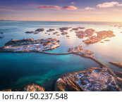 Aerial view of small islands, bridge over the sea and snowy mountains. Lofoten, Norway. Henningsvaer at sunset in winter. landscape with blue water, sky with clouds, rocks, buildings, road. Top view. Стоковое фото, агентство Ingram Publishing / Фотобанк Лори