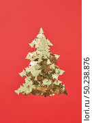 New Year decorative tree handmade from shiny small spruces on a red background, copy space. Greeting holiday card.. Christmas tree handmade from sparkly small spruces. Стоковое фото, агентство Ingram Publishing / Фотобанк Лори
