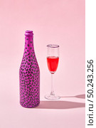 Glass of red wine with bottle painted hot pink with black spots and hard shadows on a pastel pink background, copy space.. Open bottle painted black spots with glass of red wine with shadows. Стоковое фото, агентство Ingram Publishing / Фотобанк Лори