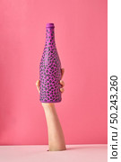 Woman’s hand holds painted bottle with black spots on a pink background, copy space.. Painted hot pink wine bottle with black spots on a pink background. Стоковое фото, агентство Ingram Publishing / Фотобанк Лори
