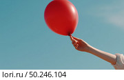 Child's hand releases a red balloon into the bright blue sky on a sunny day in a park. Стоковое AI-изображение, AI-художник Сергей Толмачёв / Фотобанк Лори