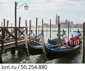 Italian traditional boats - gondolas parking near old wooden pier on the background of view of San Giorgio Maggior Church, Venice, Italy.. Traditional italian gondolas parking near berth. Стоковое фото, агентство Ingram Publishing / Фотобанк Лори
