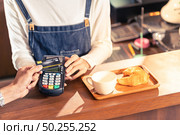 Close-up of asian customer using his credit card with contactless nfs technology to pay a barista for his coffee purchase at a cafe bar. Стоковое фото, агентство Ingram Publishing / Фотобанк Лори