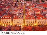 Aerial view of houses with red roofs at night in Dubrovnik, Croatia. Top view of beautiful architecture in old city. City lights, historical centre, buildings, walking people in illuminated streets. Стоковое фото, агентство Ingram Publishing / Фотобанк Лори