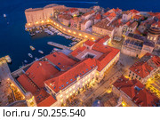 Aerial view of boats and yachts and beautiful architecture at night in Dubrovnik, Croatia. Top view of old city at sunset. Port in the sea, city lights, historical centre, buildings and red roofs. Стоковое фото, агентство Ingram Publishing / Фотобанк Лори