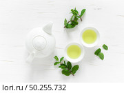 Green mint tea with fresh leaves in cups and teapot overhead on white wooden table, healthy warming drink, antioxidant beverage, top view. Стоковое фото, агентство Ingram Publishing / Фотобанк Лори