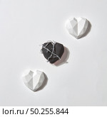Greeting Valentine’s card with three plaster hearts on a light gray background with shadows and copy space. One of them is black and wrapped twisted wire. Holiday concept.. Diagonal pattern with creative plaster hearts. Стоковое фото, агентство Ingram Publishing / Фотобанк Лори