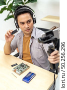 asian male IT vlogger and blogger live Technology upgrand on laptop memory ram using mobile phone recording live vlog video. Online influcencer on social media concept. Стоковое фото, агентство Ingram Publishing / Фотобанк Лори