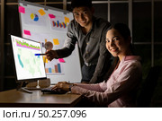 Young adult asian businessman and businesswoman work with analysis graph on white board late at night in their office with desktop computer. Using as hard working and working late concept. Стоковое фото, агентство Ingram Publishing / Фотобанк Лори