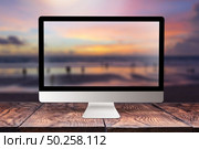 Computer display with sunset sea blurred picture on a wooden table against the same background with bokeh, copy space. Working remotely at seacoast, on nature, outside office concept.. Computer screen with blurred sea background. Стоковое фото, агентство Ingram Publishing / Фотобанк Лори