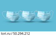 Pattern from three flying medical antibacterial protective blue face masks above blue background, copy space. Concept of prevention from respiratory sickness and viruses.. Three floating medical masks above blue background with shadows. Стоковое фото, агентство Ingram Publishing / Фотобанк Лори