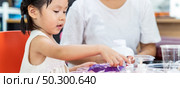 Panoramic asian girl kid playing colorful paper for art lesson at living room in home as home schooling while city lockdown because of covid-19 pandemic across the world with quaratine mom as teacher. Стоковое фото, агентство Ingram Publishing / Фотобанк Лори