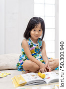 Asian girl child reading interactive book in living room at home as home schooling while city lockdown because of covid-19 pandemic across the world. Home Scholling prepare for Preschool concept. Стоковое фото, агентство Ingram Publishing / Фотобанк Лори