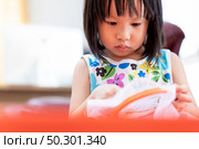 Asian girl child sewing in living room at home as home schooling while city lockdown because of covid-19 pandemic across the world. Home Scholling prepare for Preschool concept. Стоковое фото, агентство Ingram Publishing / Фотобанк Лори