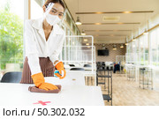 Portrait attractive asian waitress wear face mask and face shield cleaning table with alcohol and wet wipe before welcome customer. New normal hygiene restaurant concept. Стоковое фото, агентство Ingram Publishing / Фотобанк Лори