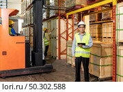 Portrait of Asian warehouse manager hold digital tablet with warehouse worker operate forklift to check inventory in background. Reopening business warehouse technology and logistic concept. Стоковое фото, агентство Ingram Publishing / Фотобанк Лори