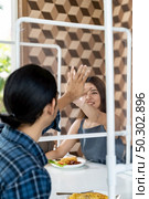 Asian young couple eating out together at new normal social distance restaurant with table shield partition reduce infection of coronavirus covid-19 pandemic. Restaurant new normal lifestyle. Стоковое фото, агентство Ingram Publishing / Фотобанк Лори