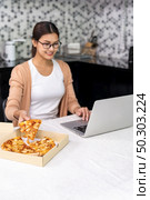 Asian woman work from home in the kitchen and eating delivery pizza take away food and take out coffee while city lockdown from coronavirus covid-19 pandemic. New Normal lifestyle working from home. Стоковое фото, агентство Ingram Publishing / Фотобанк Лори