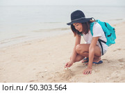 Young woman with backpack sitting on beach and try to make a castle sand. Стоковое фото, агентство Ingram Publishing / Фотобанк Лори