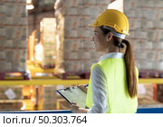 Side view of asian female warehouse worker with archboard flip chart look inventory with dustrubution warehouse in background. Reopening business warehouse technology and logistic concept. Стоковое фото, агентство Ingram Publishing / Фотобанк Лори