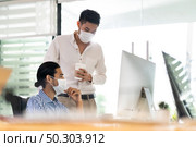 Two asian businessman talk discuss their work in morning after office reopen due to coronavirus COVID-19 pandemic. They wear protective face mask to prevent infection. New normal office life concept. Стоковое фото, агентство Ingram Publishing / Фотобанк Лори