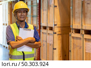 Portrait of Asian warehouse worker with clipboard job cross arm in large distribution warehouse background. Reopening business warehouse inventory and logistic concept. Стоковое фото, агентство Ingram Publishing / Фотобанк Лори