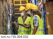 Interracial team Asian African and Caucasian work check goods use clipboard barcode scanner in distribution center. They wear face mask prevent from COVID-19. Storeroom warehouse inventory concept. Стоковое фото, агентство Ingram Publishing / Фотобанк Лори
