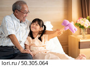 Eight years old girl playing teddy doll with dad in bed in patient ward. Mature asian father encourage her daughter after admission to in patient department in hospital. Стоковое фото, агентство Ingram Publishing / Фотобанк Лори