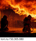 Firefighters using water fog fire extinguisher to fighting with the fire flame in large building. Firefighter and industrial safety disaster and public service concept. Стоковое фото, агентство Ingram Publishing / Фотобанк Лори