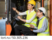 Female young asian warehouse forklift workers discuss about inventory to male warehouse manager in large distrubution warehouse background. Reopening business warehouse inventory and logistic concept. Стоковое фото, агентство Ingram Publishing / Фотобанк Лори