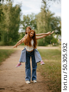Younger sister rides on older sister's back in the park. Стоковое фото, фотограф Юлия Потапова / Фотобанк Лори