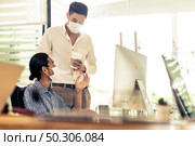 Two asian businessman talk discuss their work in morning after office reopen due to coronavirus COVID-19 pandemic. They wear protective face mask to prevent infection. New normal office life concept. Стоковое фото, агентство Ingram Publishing / Фотобанк Лори
