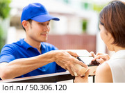 Asian woman sign electronic signature to portable mobile device after receive package from male delivery man in blue shirt. Package shopping delivery and digital sign concept. Стоковое фото, агентство Ingram Publishing / Фотобанк Лори