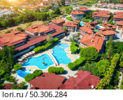 Aerial view of hotel, pool, swimming people in transparent blue water, umbrellas, sunbeds, green trees at sunset. Summer holidays. Top view of buildings. Relax and leisure in luxury resort in Europe. Стоковое фото, агентство Ingram Publishing / Фотобанк Лори