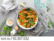 Chicken drumsticks roasted with vegetables in cast iron pan on kitchen table, top down view. Стоковое фото, агентство Ingram Publishing / Фотобанк Лори