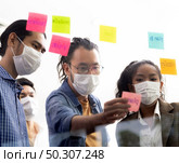 Interracial asian business team brainstorming idea at office meeting room after reopen due to coronavirus COVID-19 city lockdown. They wear face mask reduce risk to infection as new normal lifestyle. Стоковое фото, агентство Ingram Publishing / Фотобанк Лори