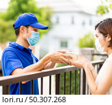 Asian deliver man in blue shirt handling package and give to young woman costumer at house. They wear face mask to reduce coronavirus COVID-19 spreading. Package shopping delivery concept. Стоковое фото, агентство Ingram Publishing / Фотобанк Лори